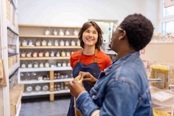 Eco-friendly grocery shop owner assisting a female customer. Store clerk helping woman customer at sustainable plastic free shop.