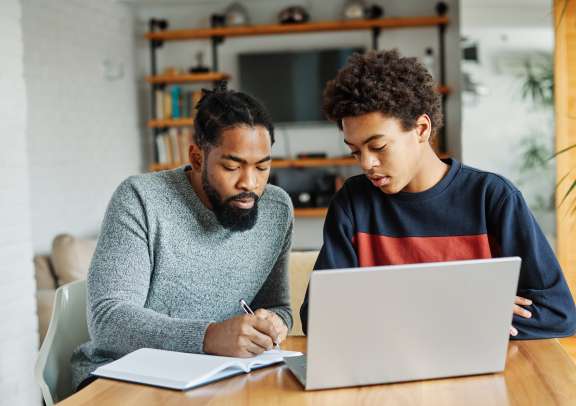 Father and son doing homework with laptop at home. Father and teenage son using laptop. Boy and dad sitting at home working with notebook