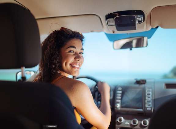 A woman smiling while driving her car, showcasing a joyful and confident expression behind the wheel.