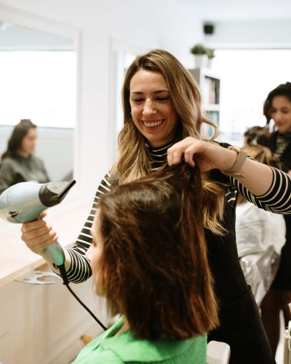 Woman hairstylist blowdrying client cropped