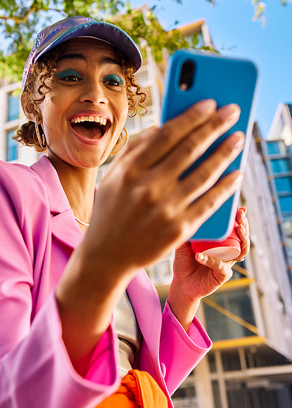A woman dressed in a pink jacket and hat poses for a selfie, looking cheerful.